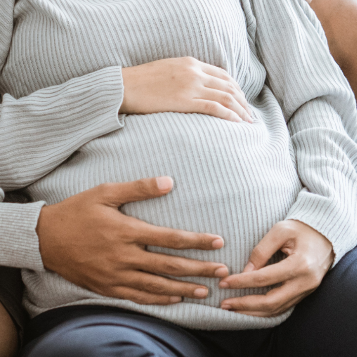 Schwangere, die dahinter sitzende Person legt die Hand auch den  Bauch