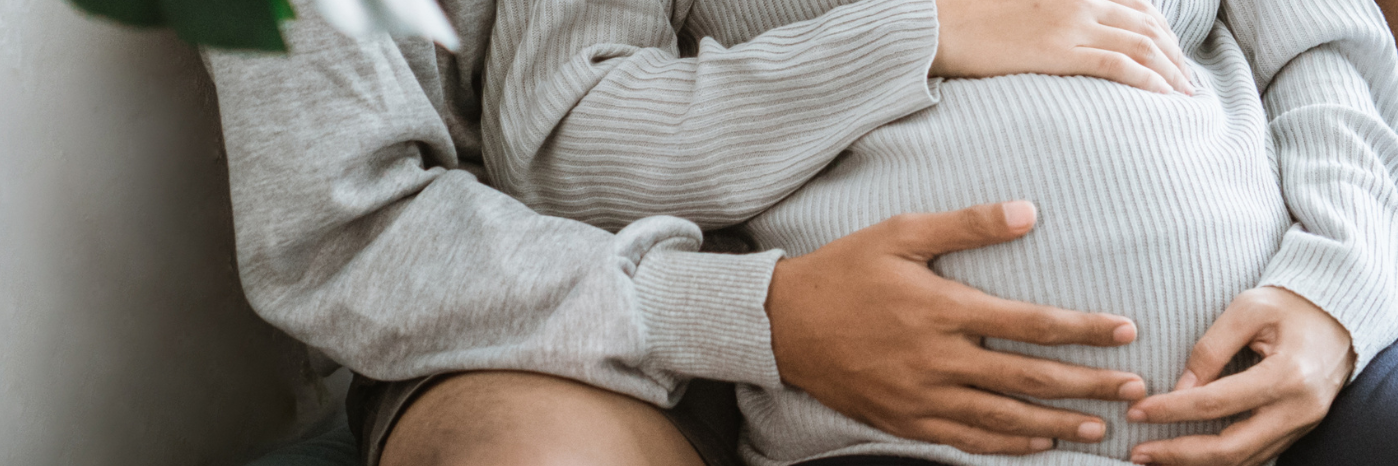 Schwangere, die dahinter sitzende Person legt die Hand auch den  Bauch