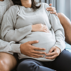 Schwangere, die dahinter sitzende Person legt die Hand auch den  Bauch
