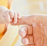 eine Baby Hand umfasst den Finger eines Erwachsenen