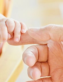 eine Baby Hand umfasst den Finger eines Erwachsenen