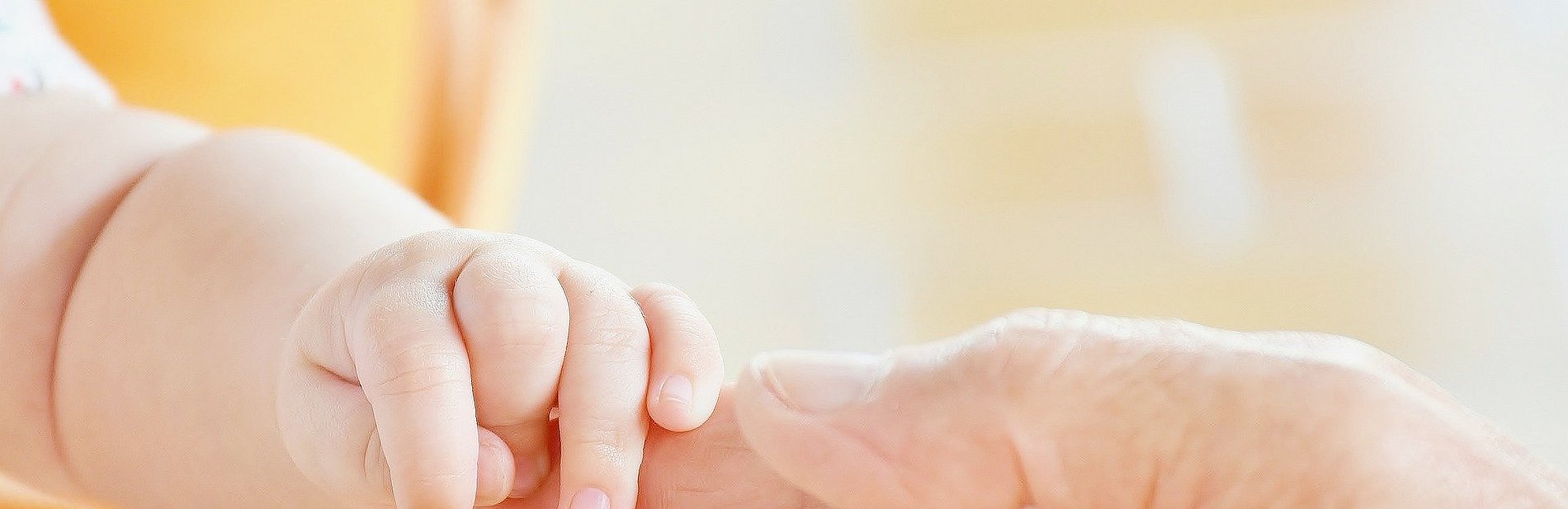eine Baby Hand umfasst den Finger eines Erwachsenen