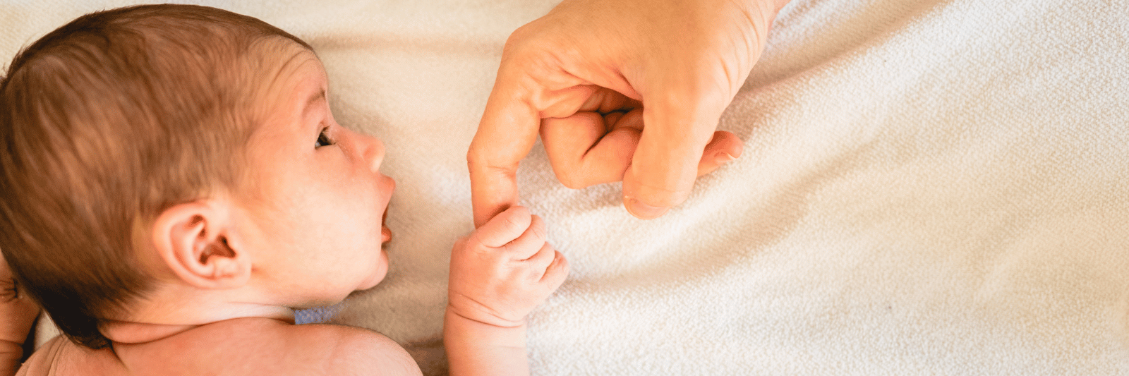 ein neugeborenes Baby liegt auf dem Bauch, schaut zur Seite und hält den Finger eines Erwachsenen