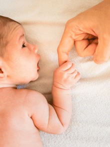 ein neugeborenes Baby liegt auf dem Bauch, schaut zur Seite und hält den Finger eines Erwachsenen