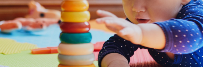 Baby liegt auf dem Bauch und greift nach Spielzeug