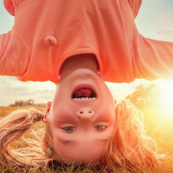 ein junges Mädchen mit Zöpfen, die Kopfstand auf einer Sommerwiese bei tiefstehender Sonne macht