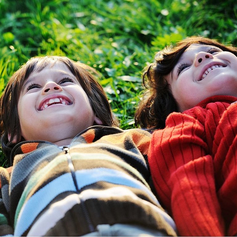 zwei kinder liegen nebeneinander im Gras und schauen in den Himmel
