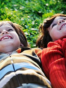 zwei kinder liegen nebeneinander im Gras und schauen in den Himmel