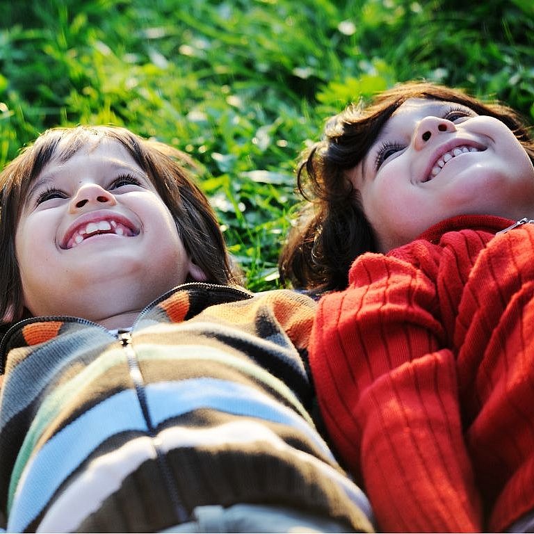 zwei kinder liegen nebeneinander im Gras und schauen in den Himmel