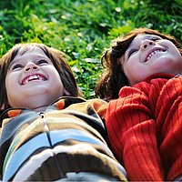zwei kinder liegen nebeneinander im Gras und schauen in den Himmel
