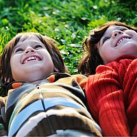 zwei kinder liegen nebeneinander im Gras und schauen in den Himmel