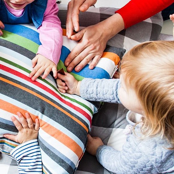 mehrere Kinder und Erwachsenenhände auf einem Kissen