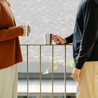 zwei menschen stehen sich an einem Geländer gegenüber. man sieht die Gesichter nicht, sie halten jeweils einen Becher in der Hand.